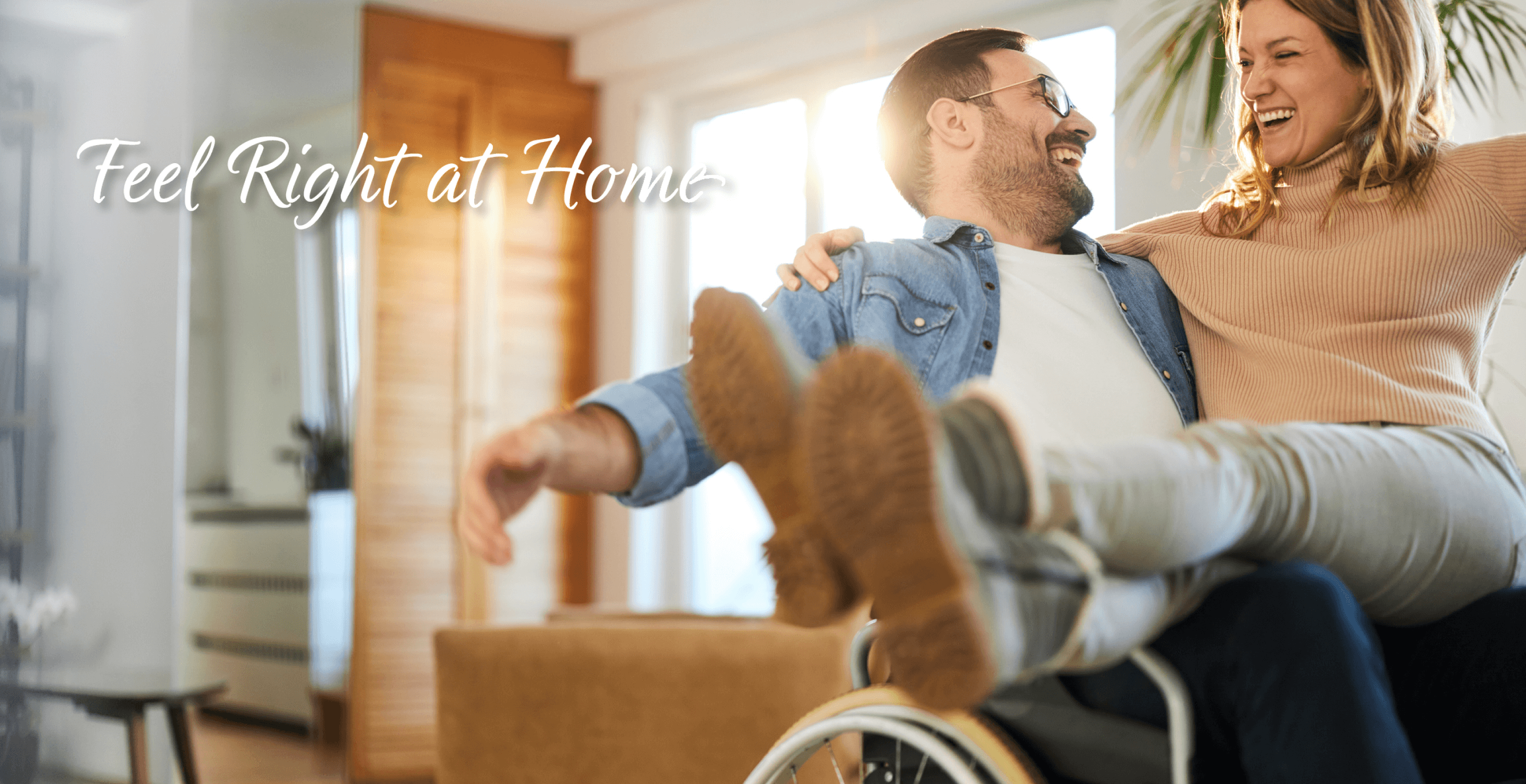 A man in a wheelchair laughing with his partner in a bright, cozy living space, representing comfort and independence.